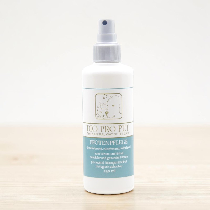 Flacone spray bianco Bio Pro Pet per la cura delle zampe su un tavolo di legno chiaro su sfondo bianco. Etichetta blu con cane e gatto: disinfettante, idratante, rinforzante, a pH neutro, senza solventi, biodegradabile. 250 ml.