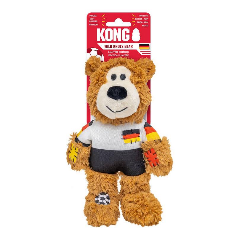 Peluche marrone a forma di orso, con maglia da calcio bianca e pantaloncini neri nei colori della nazionale tedesca. Zampe decorate con toppe colorate e motivi calcistici. Il giocattolo è appeso a una confezione rossa Kong.