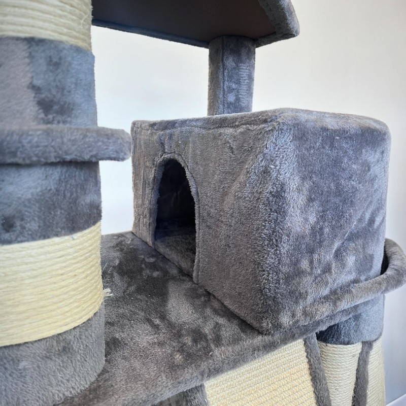 Ein mehrstufiger, großer Kratzbaum aus weichem, grauem Plüschstoff. Eine gemütliche Katzenhöhle mit rundem Eingang ist zentral platziert. Robuste Säulen, teils mit hellem Sisalseil, bieten Kratzmöglichkeiten.