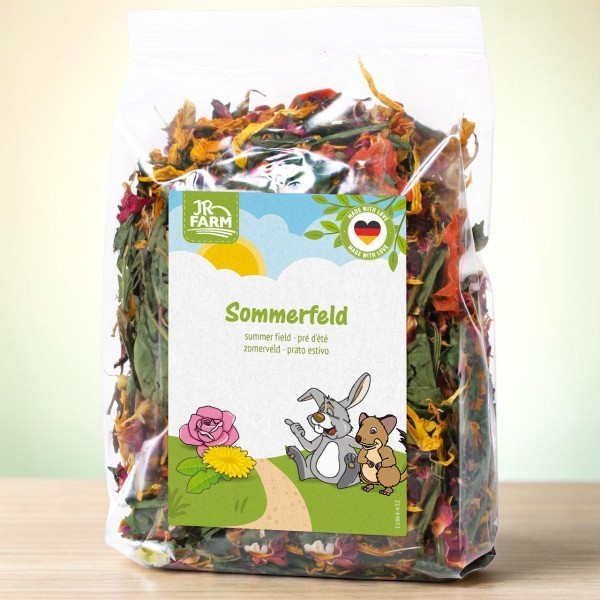 Transparenter Beutel mit bunter Mischung aus getrockneten Blüten und Kräutern: rote Rosenblätter, gelbe Ringelblumen, grüne Pflanzenfasern. Weißes Etikett: „Sommerfeld“ mit Kaninchen und Hamster auf Wiese.
