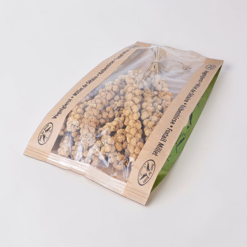 Brins de millet à épis jaunes dans un emballage transparent. Ce millet séché, à la texture granuleuse, est conditionné dans un sachet écologique aux bords marron et verts. Friandise naturelle et divertissante pour oiseaux.
