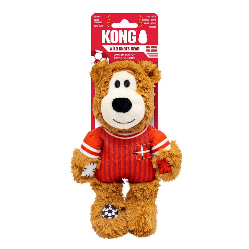 Orsacchiotto di peluche con pelo marrone e maglia da calcio a strisce rosse e bianche. Sul petto una croce bianca, sulle maniche strisce bianche. Muso chiaro, occhi neri, muso ricamato. Zampe/piedi con toppe, motivo a palloni da calcio.