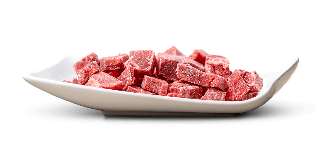 Cubetti di carne congelata di colore rosso intenso giacciono in un vassoio bianco, allungato e leggermente ricurvo. Le loro superfici sono ricoperte da sottili cristalli di ghiaccio. Isolati su uno sfondo bianco chiaro.