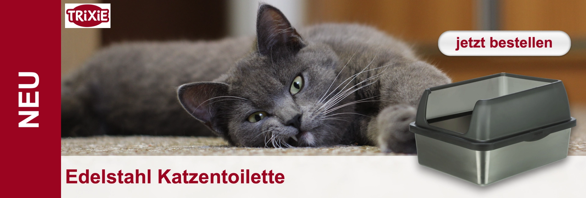 Grauer Kater liegt entspannt auf beigem Teppich und blickt mit grünen Augen in die Kamera. Rechts daneben eine Edelstahl-Katzentoilette mit dunkelgrauer Haube. Links auf Rot steht "NEU", unten "Edelstahl Katzentoilette". TRIXIE-Logo oben links.