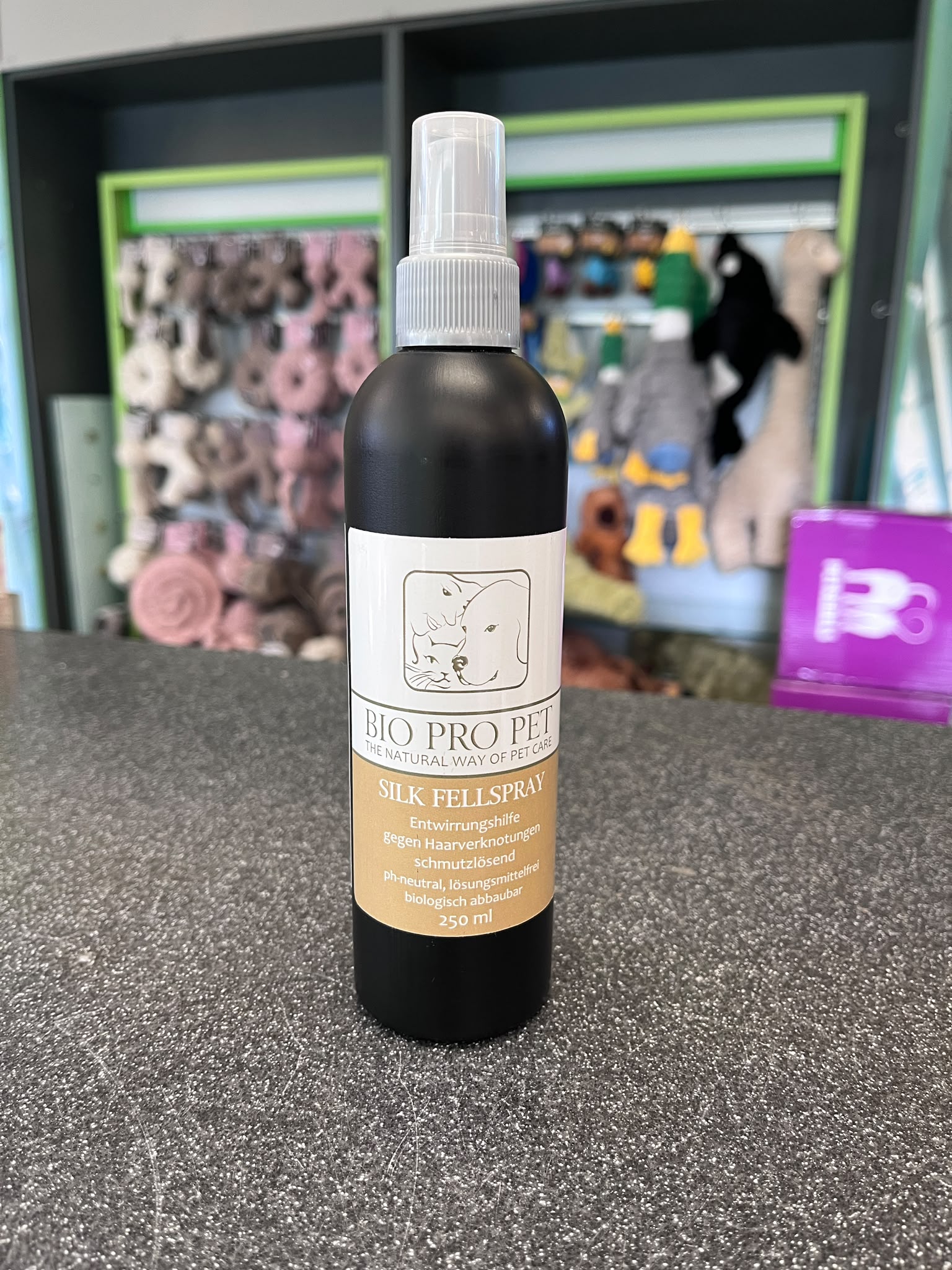 Flacon pulvérisateur noir de 250 ml « Bio Pro Pet » avec tête de pulvérisation blanche sur fond foncé moucheté. Étiquette couleur crème : « SILK FELLSPRAY », aide au démêlage, élimine les salissures, pH neutre, biodégradable.