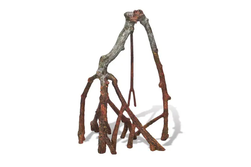 Skulpturale Anordnung von Ästen oder Wurzeln auf weißem Hintergrund. Zwei dicke, hellgraue Äste bilden oben eine Brücke und verzweigen sich nach unten in zahlreiche dünnere, rötlich-braune Stützen. Ein schlanker dunkler Stab stabilisiert.