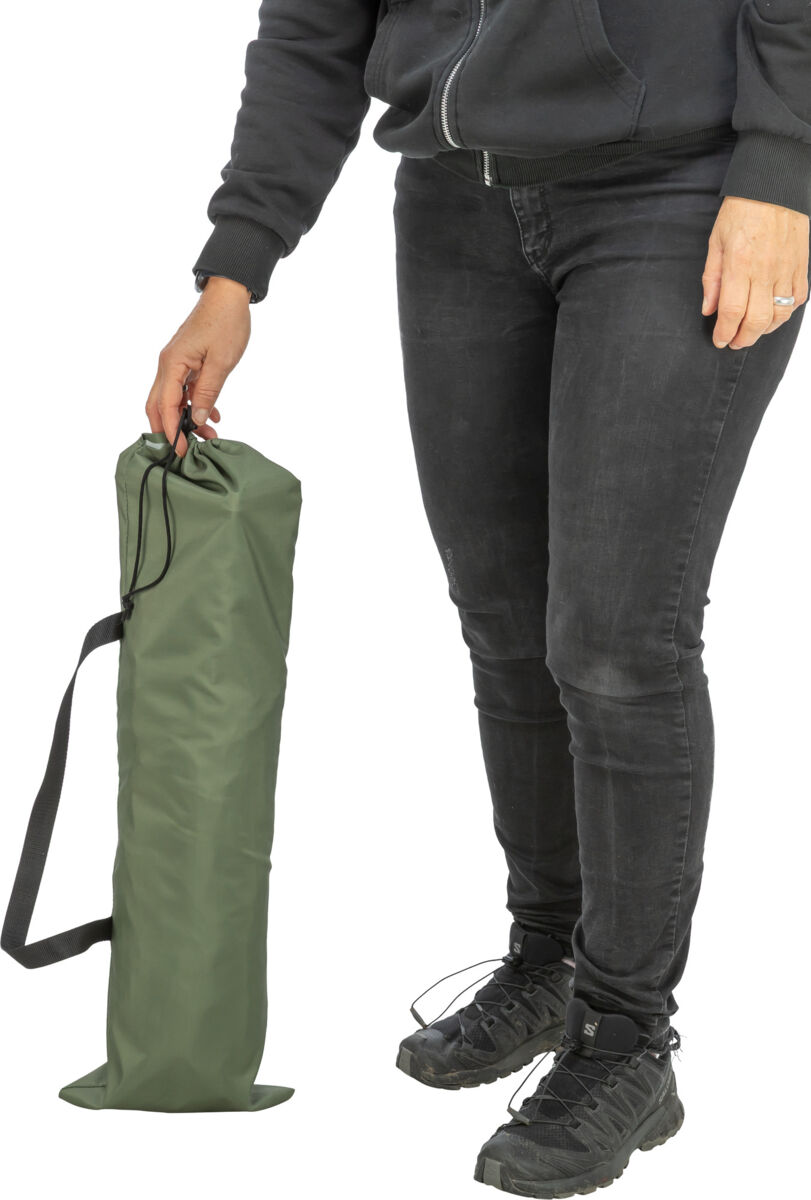 Una persona con una felpa scura con cappuccio e jeans tiene in mano, sulla destra, un sacco da viaggio cilindrico di colore verde oliva con cordoncino nero. Il sacco da viaggio ha una tracolla nera ed è posizionato in verticale accanto alle gambe.