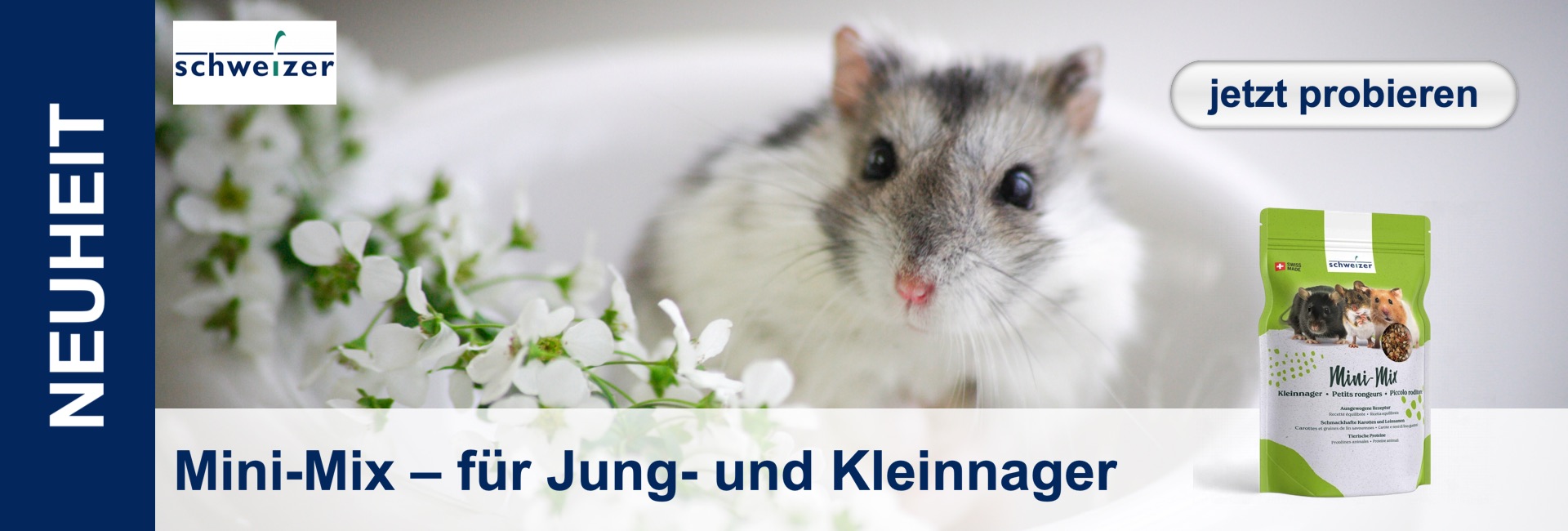 Un criceto con la pelliccia grigia e bianca siede accanto a fiori bianchi, mentre sulla destra c'è un sacchetto di cibo.