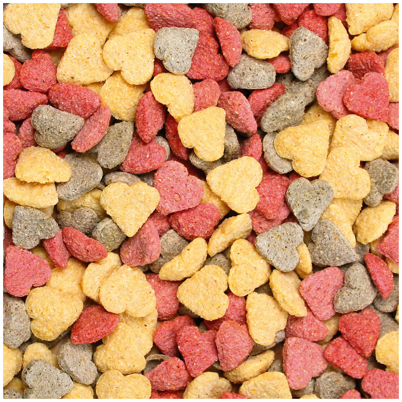 Pellets colorati di mangime secco per animali domestici, disposti fitti fitti. I granelli sono prevalentemente gialli, rossi e grigi e hanno forme diverse, tra cui piccoli cuori e pezzi irregolari che ricoprono la superficie.