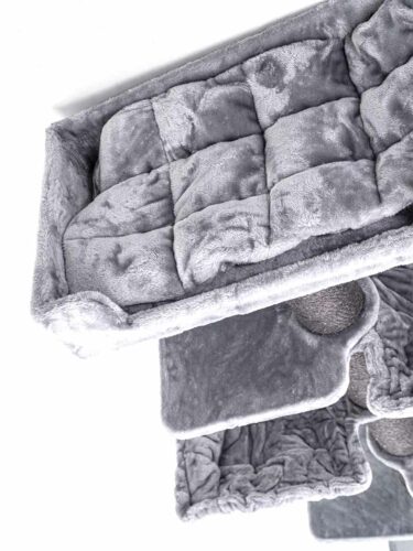 Morbida trapunta grigia con motivo a quadrati trapuntati, sovrapposti su fondo bianco. Soffice e leggermente strutturata, ne sottolinea l'imbottitura. Il bordo grigio chiaro ai margini ne evidenzia lo spessore e il comfort.