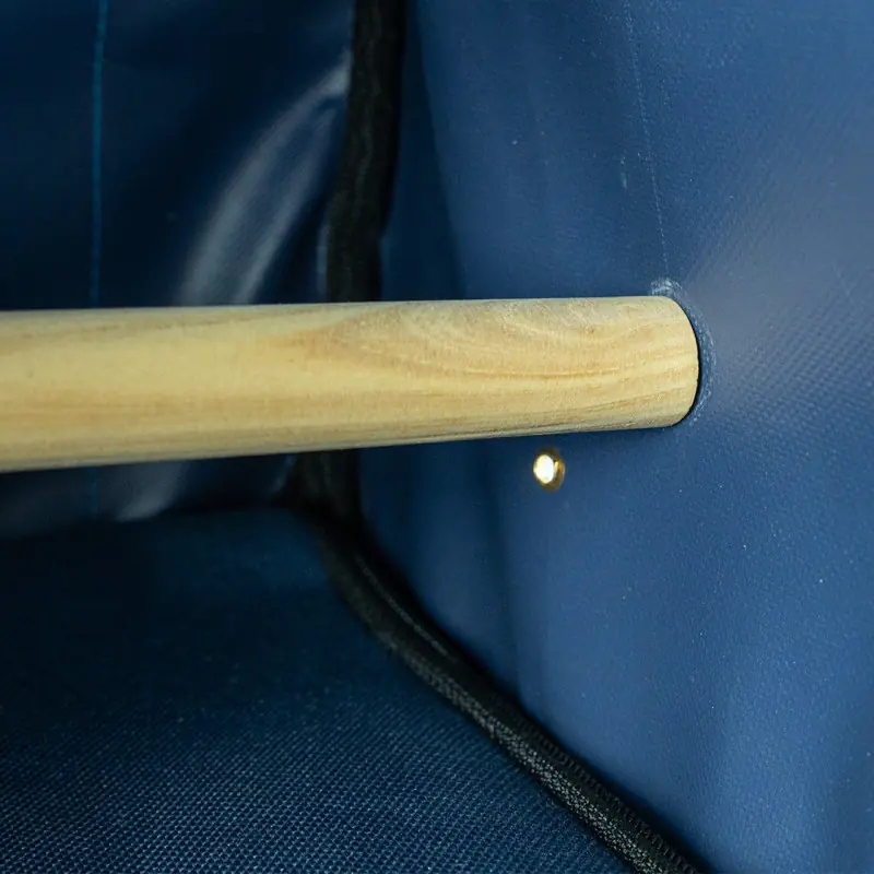 Close-up of a wooden rod in a round hole in a blue fabric wall. A light source is visible next to it.