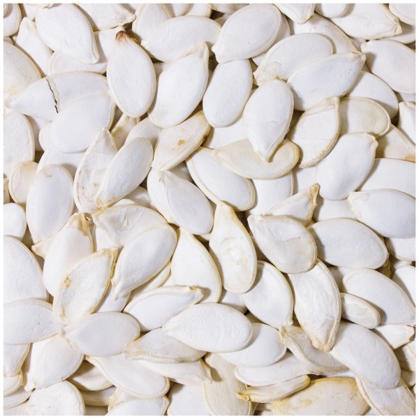 A dense cluster of white, oval pumpkin seeds filling the entire frame. The seeds range in colour from light cream to white, with a slightly glossy surface, and some show fine cracks or irregular shapes.