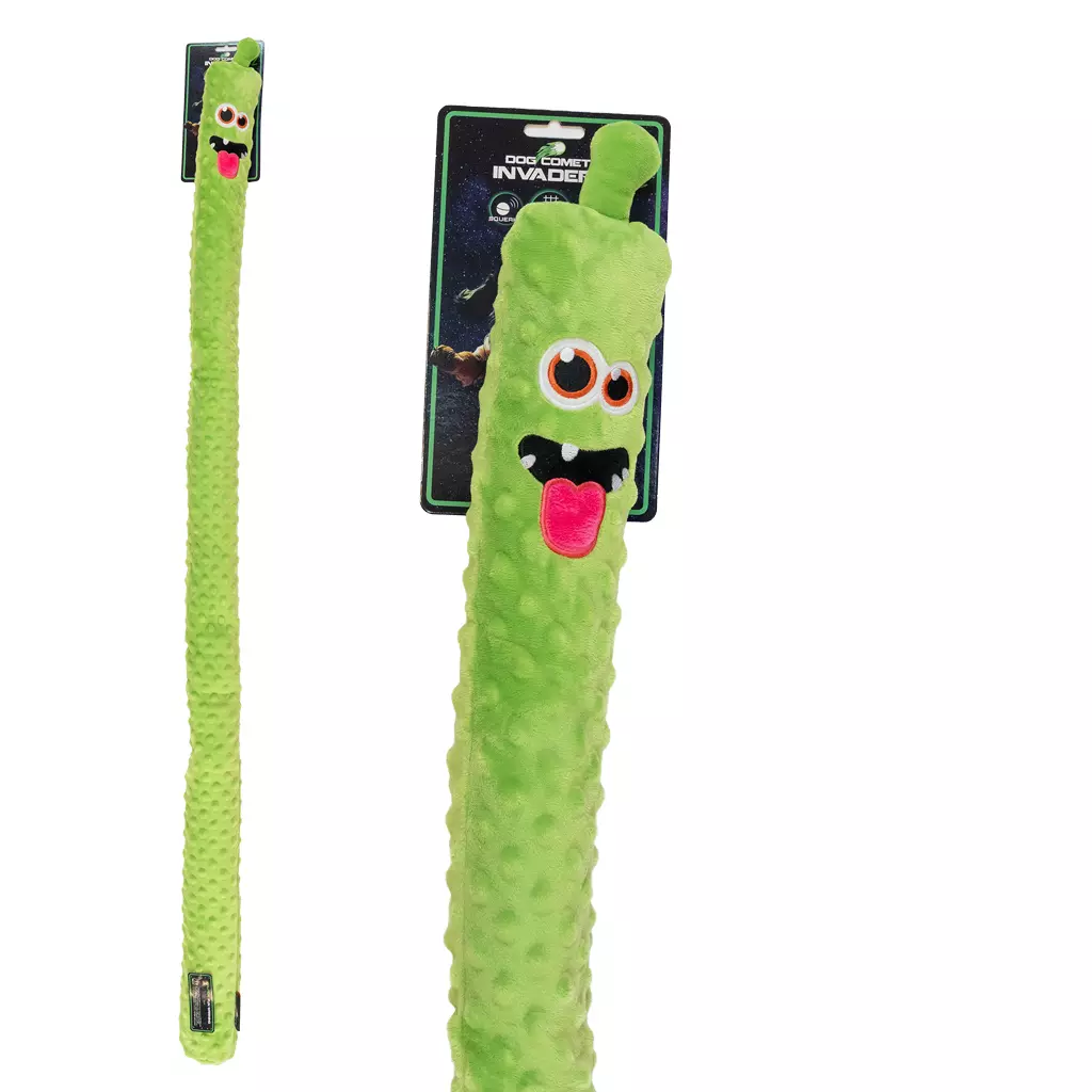 Lungo giocattolo per cani in peluche verde a forma di mostro. Superficie a rilievi, grandi occhi contornati di arancione, due piccoli denti e lingua rosa protesa. Fissato a una confezione nera con la scritta "DOG COMET INVADER".