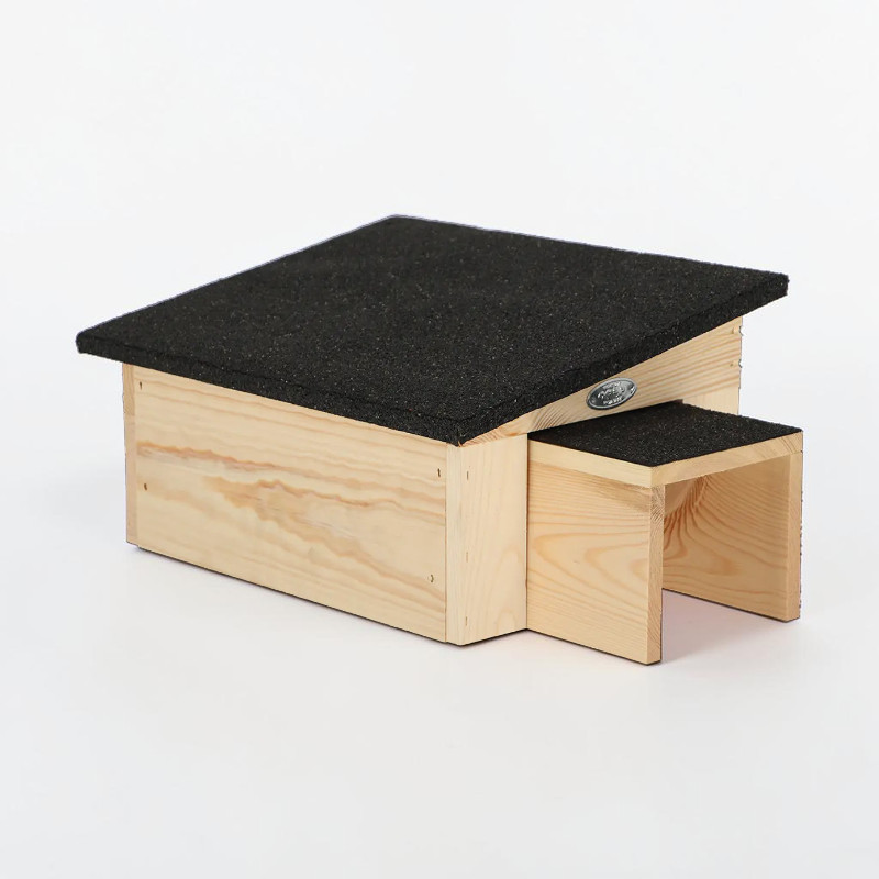 Maison pour hérissons en bois d'épicéa clair avec toit incliné en bitume foncé. Allongée, avec entrée latérale, elle offre un refuge protégé pour se reposer, se cacher et hiberner dans les jardins naturels.