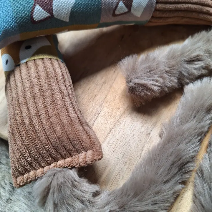 Nahaufnahme eines Stofftiers mit Cord-Körper, Musterdruck und flauschigem Fell auf hellem Holzgrund.