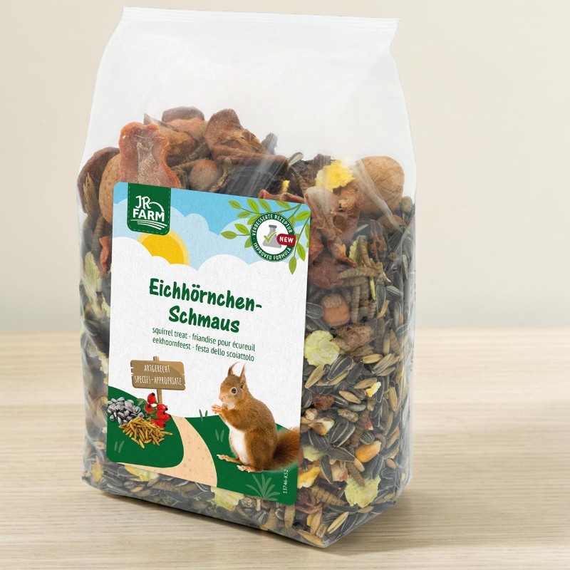 Transparent plastic bag of mixed squirrel feed on a light-coloured wooden surface. Contains sunflower seeds, nuts, dried fruit and insects. Colourful label: ‘Squirrel Feast’ featuring a squirrel.