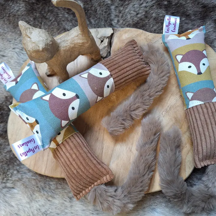 Handgefertigtes Katzenspielzeug in Fuchsform, mit Schwanz, auf Holzbrett. Im Hintergrund steht eine kleine Katzenfigur.