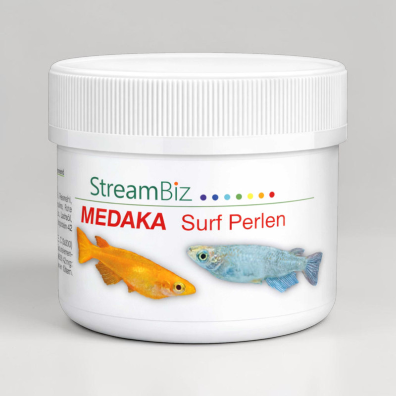 Boîte à nourriture blanche et ronde pour poissons, avec bouchon à vis nervuré. Étiquette : Streambiz (vert), MEDAKA Surf Perlen (rouge). Deux poissons (orange doré, bleu clair) nagent parmi des granulés flottants.