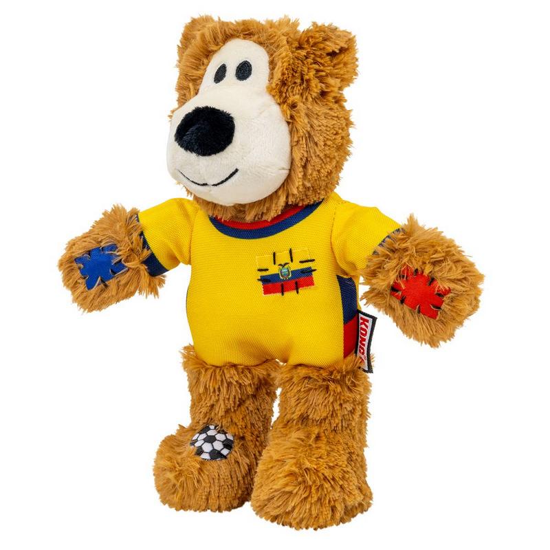 Morbido orsacchiotto marrone con muso chiaro, naso nero e sorriso. Indossa maglia da calcio gialla con colletto e polsini blu/rossi, bandiera Ecuador sul petto. Toppe blu/rosse, pallone sul piede sinistro, etichetta Kong rossa.