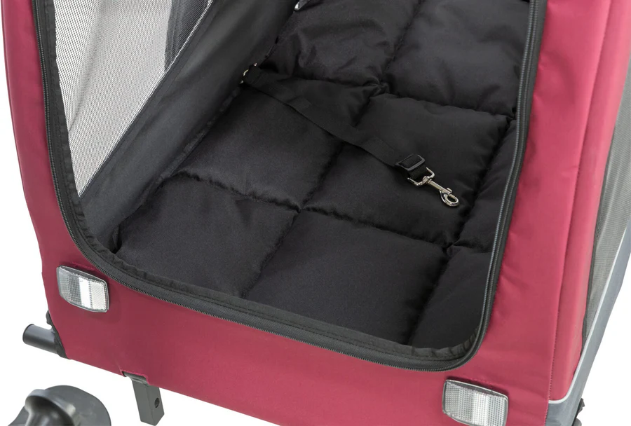 Offener Innenraum eines dunkelroten Haustiertrailers/-buggys mit weicher, schwarzer, gesteppter Matte. Schwarzes Sicherungsband mit silbernem Karabiner an der Seite. Netzwand und Reflektor für sicheren, bequemen Transport.