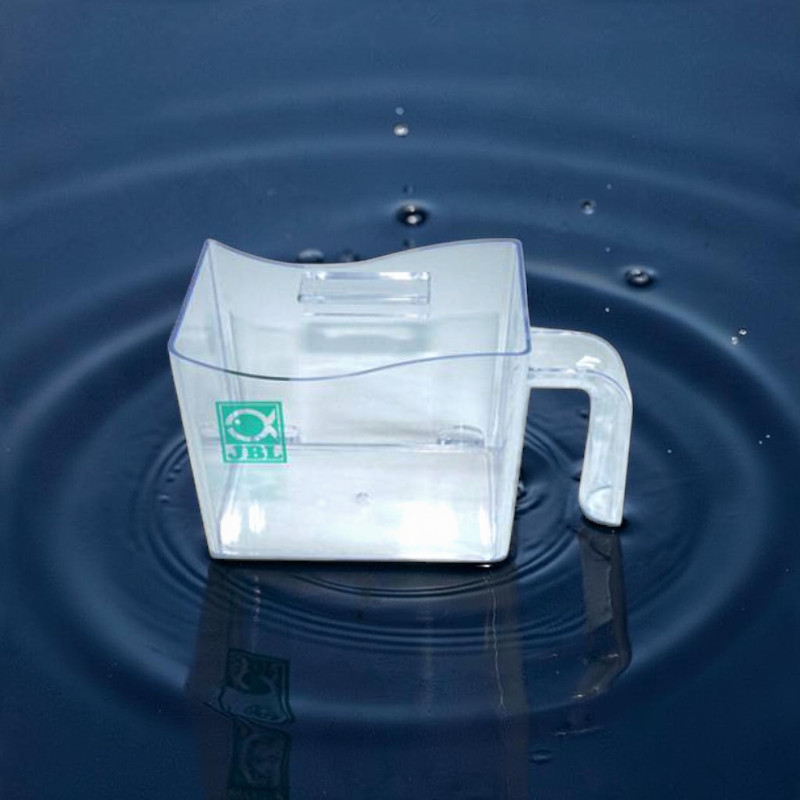 Ein transparenter, eckiger JBL Fischfangbecher mit Griff ist in dunkles blaues Wasser getaucht. Vom Becher gehen konzentrische Wellen aus, Wassertropfen sind in der Luft sichtbar. Das grüne JBL-Logo mit Fischsymbol ist erkennbar.
