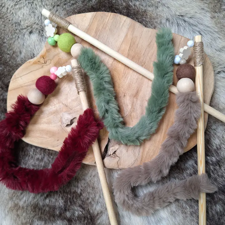 Drei Katzenangeln in rotbraun, grün und grau mit Holzstab und Fell auf einem Holzbrett. Dekoriert mit Holzperlen und Filzkugeln.