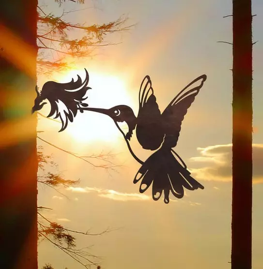 Silhouette d'un colibri sur un arbre. Design de fiche d'arbre en métal devant un ciel ensoleillé. Sculpture de jardin décorative.