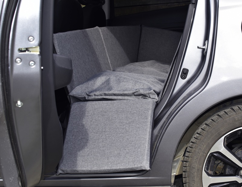 Lit pour chien Goro gris, installé en toute sécurité à l'arrière d'une voiture grise, avec la portière ouverte laissant entrevoir le lit moelleux. Des parois latérales hautes et un coussin douillet, idéal pour voyager avec son chien.