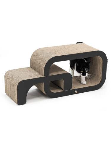 Un gatto bianco e nero osserva con curiosità da un tiragraffi beige in cartone ondulato con cornice nera. Questo moderno tiragraffi ha una forma sinuosa a gradini e offre al gatto un passaggio. Il gatto ha zampe e muso bianchi.