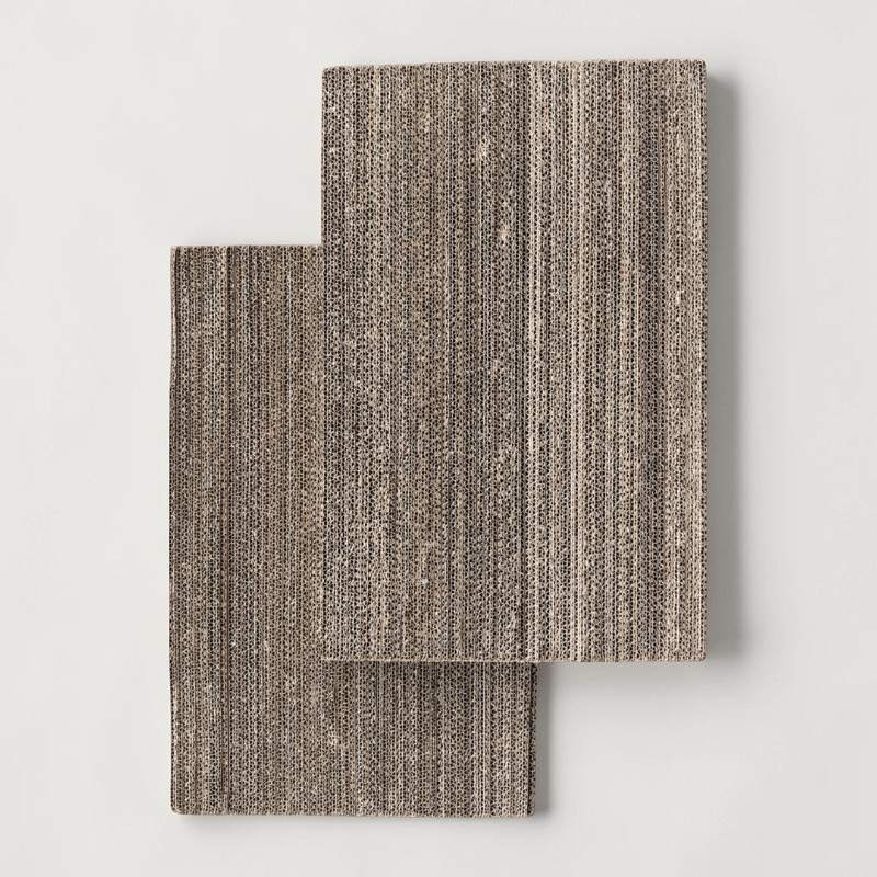 Two rectangular fabric pieces with a fine, vertically striped pattern in shades of brown and black overlap slightly against a light-coloured background. The top piece is positioned on the right, the bottom piece on the left, and protrudes slightly.
