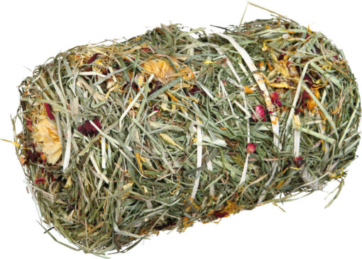 Ein länglicher, zylinderförmiger Heu- und Kräuterballen liegt vor weißem Hintergrund. Er besteht aus getrocknetem grünem Gras mit hellgelben, cremefarbenen Blütenköpfen und vereinzelten roten Blütenblättern.