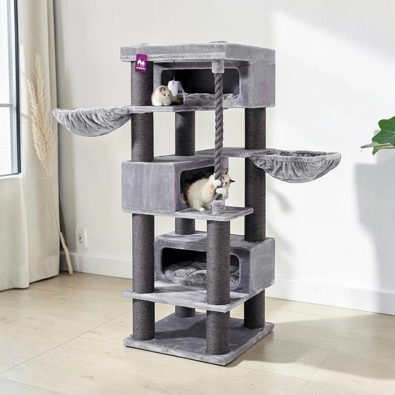 A large, multi-level cat tree in grey with sisal posts, caves and hammocks in a bright room. A light-coloured cat is resting at the top. A second cat with light-coloured fur is using a scratching post in a lower cave. Ideal for climbing and playing.