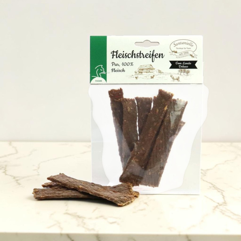 Ein transparenter Beutel mit getrockneten, dunkelbraunen Fasan-Fleischstreifen steht auf heller Marmorfläche. Mehrere flache, unregelmäßige Streifen liegen davor und zeigen Konsistenz und Farbe des Hundesnacks als Belohnung.