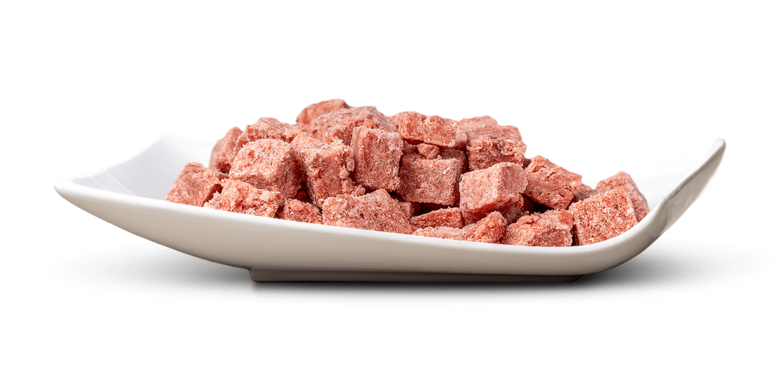 Weiße, flache Schale mit vielen kleinen, unregelmäßig geformten, rosaroten Würfeln mit leicht rauer oder pudriger Oberfläche. Die Schale steht auf reinweißem Hintergrund mit leichtem Schatten darunter; die Würfel sind dicht geschichtet.