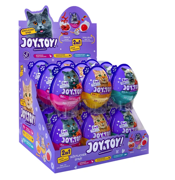 Lila Verkaufsdisplay für JOY & TOY Überraschungseier für Katzen, gefüllt mit Snacks und Spielzeug. Mehrere Katzenbilder, u.a. eine große graue Katze mit Zunge. Ovale Eier mit Sorten Ente, Huhn, Thunfisch und Toys.