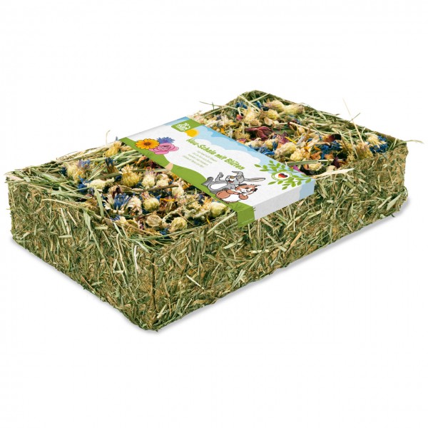 A rectangular block of compressed hay, filled with a colourful mix of dried flowers in blue, yellow and pink. A white band with a green border runs across the top, featuring two cartoon rabbits and the text ‘Hay Bowl with Flowers’.