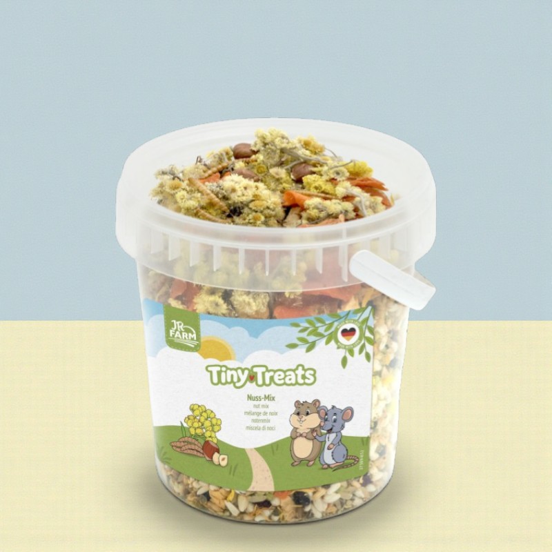 Ein durchsichtiger Behälter mit JR Farm Tiny Treats Nuss-Mix für Nager, gefüllt mit Nüssen, Gemüse und Saaten.