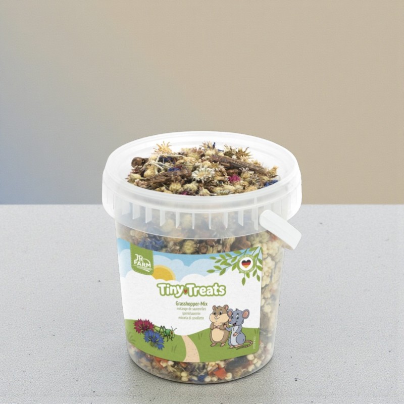 Ein transparenter Eimer mit JR Farm Tiny Treats Grasshopper-Mix, gefüllt mit Blüten, Karotten und Heuschrecken.
